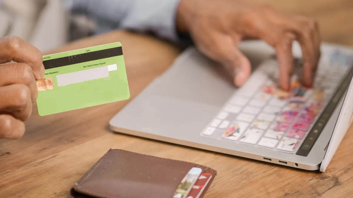 Card bancar ținut în mână lângă laptop, în timpul unei plăți online