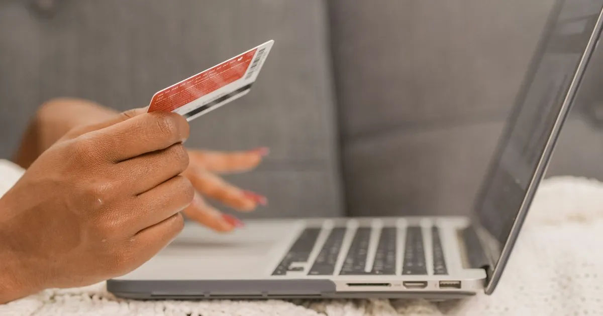 Persoană ținând un card bancar lângă laptop, în timpul unei plăți online