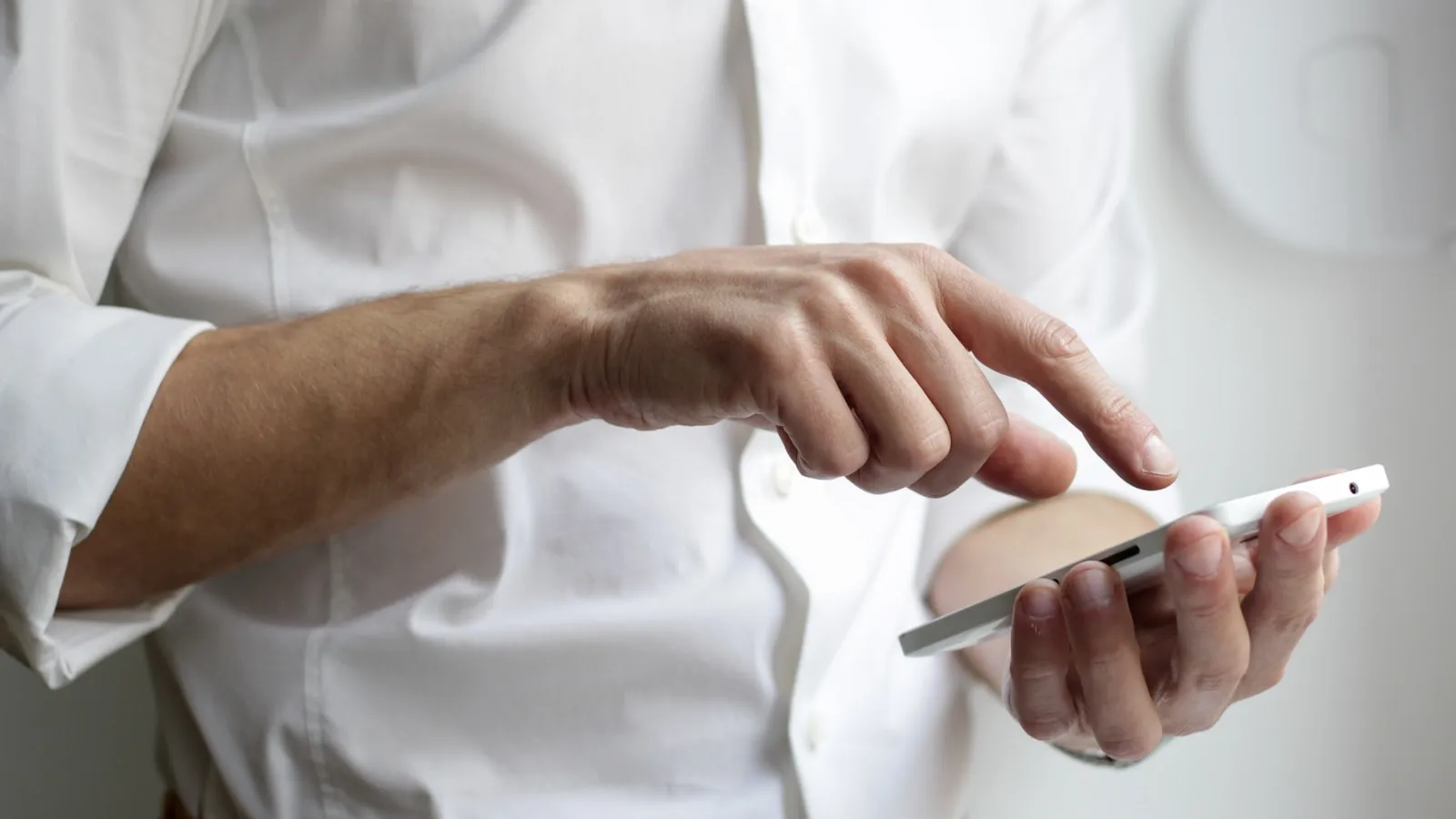 Bărbat în cămașă albă atingând ecranul unui telefon, introducând un cod de verificare