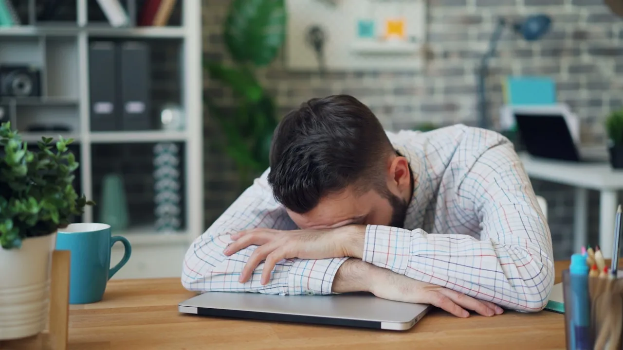 Bărbat sprijinit pe un laptop închis, copleșit, la birou