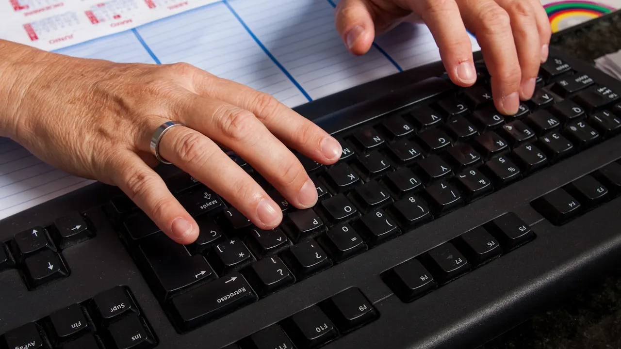 Mâini tastând pe tastatura unui calculator la birou