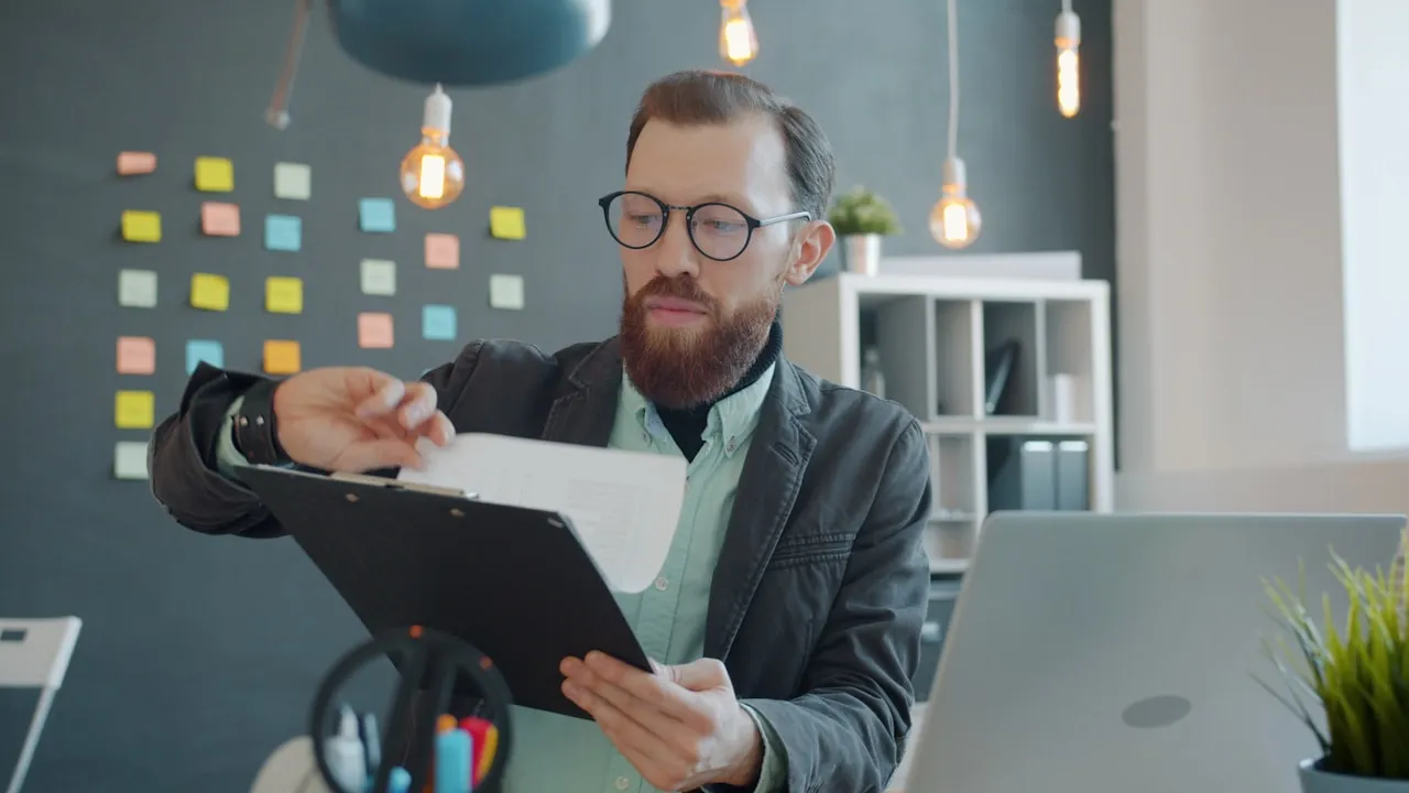 Profesionist cu ochelari verificând un document la birou, într-un birou modern