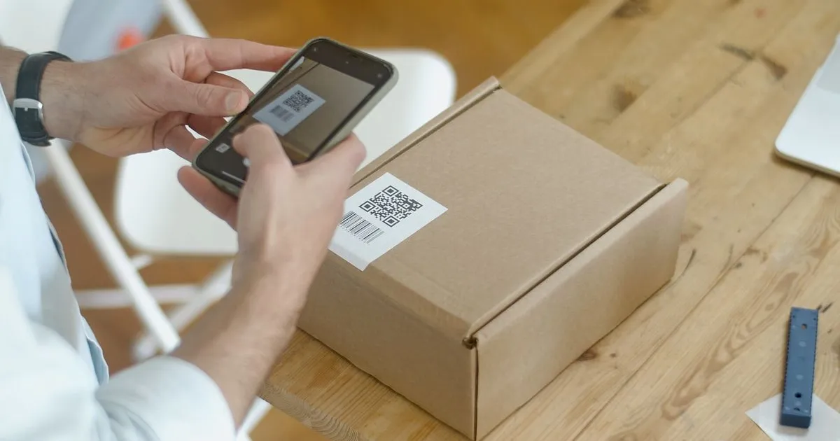 Telefon ținut deasupra unui colet, verificând o livrare