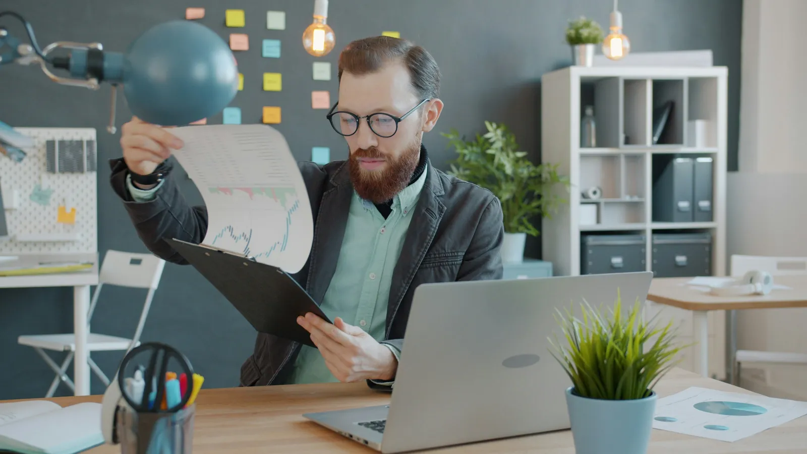 Persoană analizând documente lângă un laptop într-un birou modern