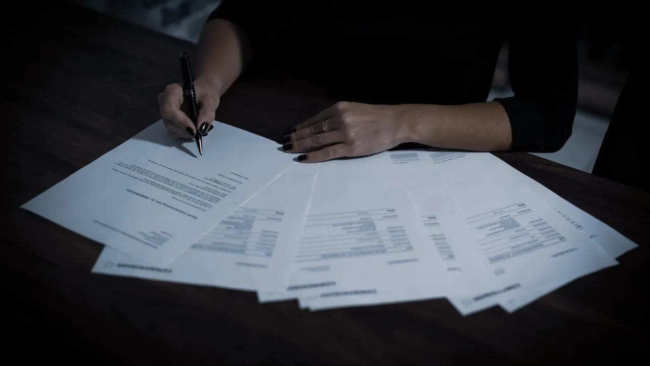 Persoană semnând un document tipărit cu pixul, pe un birou de lucru