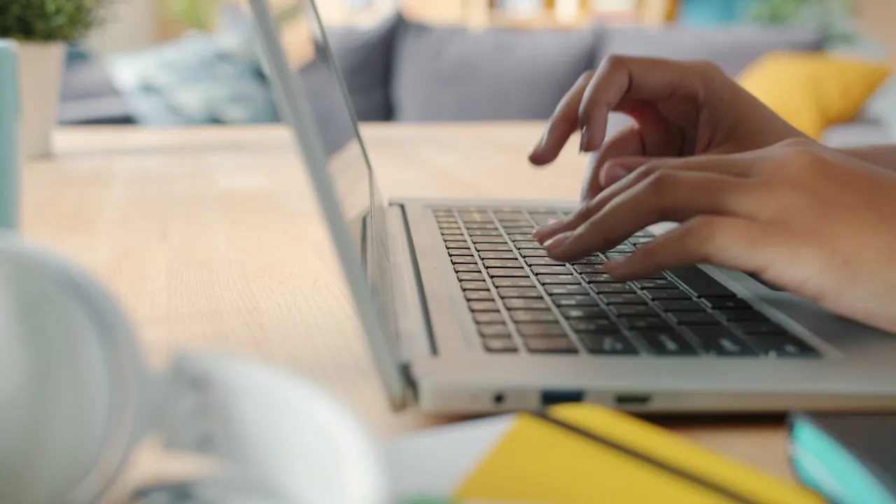 Mâini care scriu pe tastatura unui laptop la birou, în timpul contactării serviciului de suport