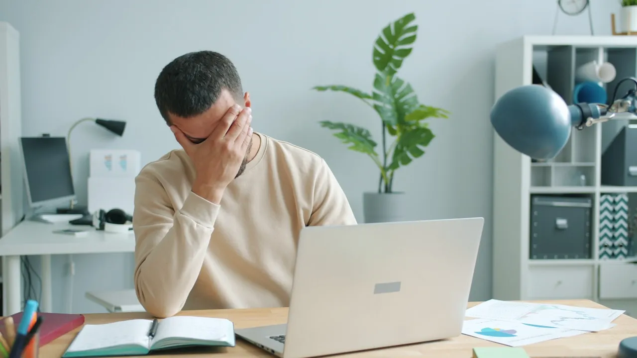 Bărbat la birou care își ține fruntea, frustrat că nu reușește să își recapete contul