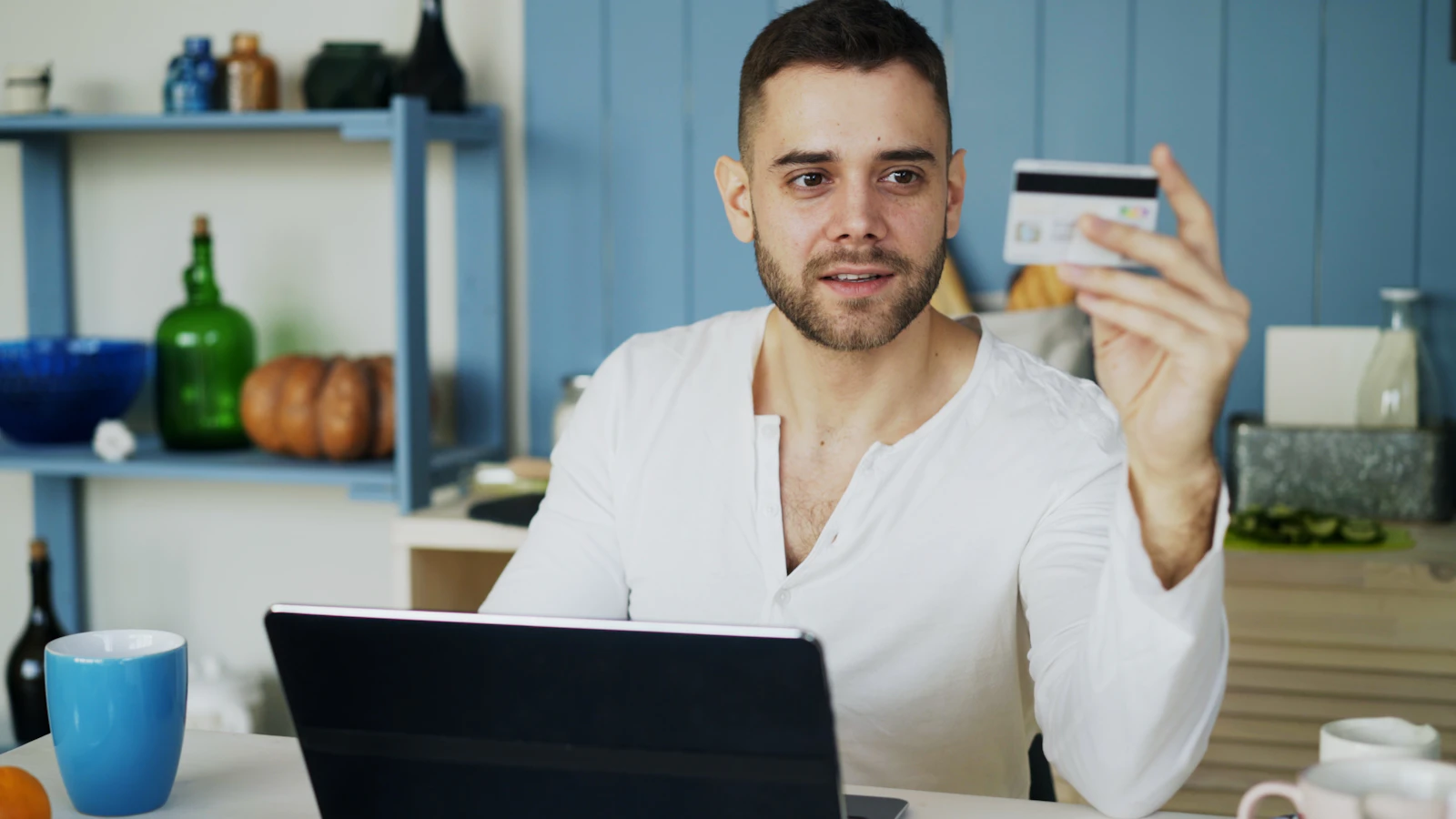 Bărbat ținând un card bancar în timp ce cumpără online de pe laptop